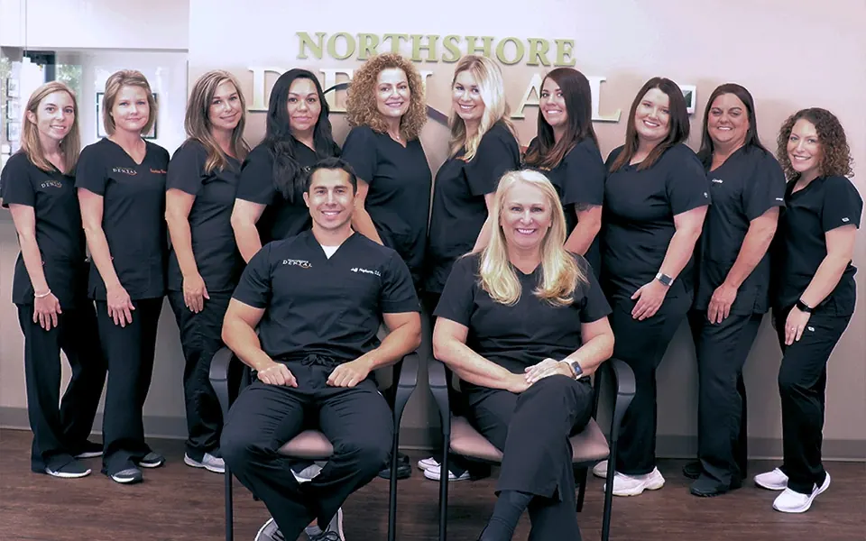 The Northshore Dental team in front of the reception sign, with Dr. Hepburn and Dr. Core seated.